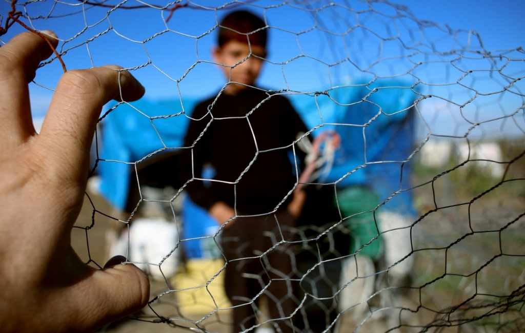 a refugee kid looking out of a refugee camp through a mesh